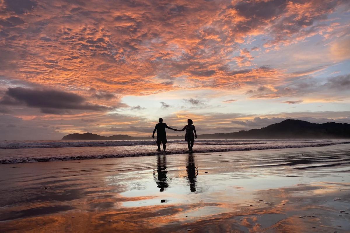 Deux silhouettes marchant les pieds dans l'eau au crépuscule sur la plage Samara